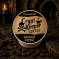 A single round coffee pod package labeled 'Crypt Keeper Coffee' and 'Caramel Nut' sits on a dark textured surface surrounded by coffee beans, with a candle and stone archway in the background.