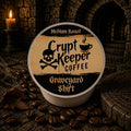 A single round coffee pod package labeled 'Crypt Keeper Coffee' and 'Graveyard Shift' sits on a dark textured surface surrounded by coffee beans, with a candle and stone background in the scene.