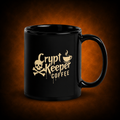 A glossy black ceramic mug with a gold-colored 'Crypt Keeper Coffee' logo featuring a skull and crossbones and a coffee cup graphic, set against a dark brown textured background.