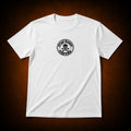 A white short-sleeve crewneck t-shirt with a circular black graphic on the left chest reading 'Crypt Krew COFFEE' around a skull and crossbones, displayed against a dark brown vignette background.
